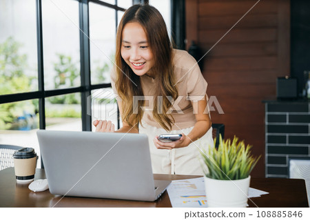 Excited woman holding mobile smart phone raising hands after playing online game and making winner gesture, young female smile got good news on smartphone while working on computer at cefa 108885846