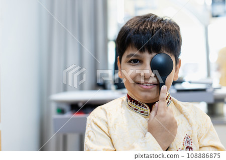Happy Indian child boy examining eyesight modern ophthalmology equipment in clinic. 108886875