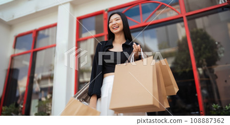 Happy beautiful young stylish woman with shopping bag while walking come out of mall on holiday Black Friday Happy beautiful young stylish woman with shopping bag while walking come out of mall on holiday Black Friday 108887362