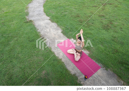Asian woman standing on fitness mat, sporty lady practicing yoga at public park outdoor, stretching her body. Healthy active lifestyle 108887367