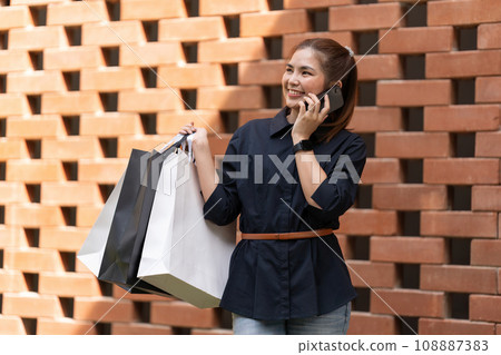 Woman using smartphone holding Black Friday shopping bag while standing on the side with the mall 108887383