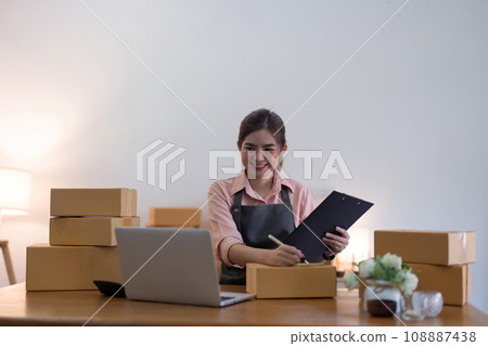 Woman is writing a list of customer on box before shipping to them, she runs an ecommerce business on websites and social media. Concept of sell product online 108887438