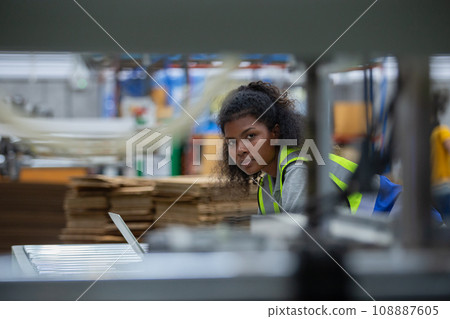 Staff worker woman american african using laptop check quality and quantity stock paper product. Staff worker woman american african using laptop check quality and quantity stock paper product. 108887605