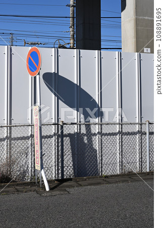 The shadow of the no parking sign on the road is reflected on the construction fence The shadow of the no parking sign on the road is reflected on the construction fence 108891695