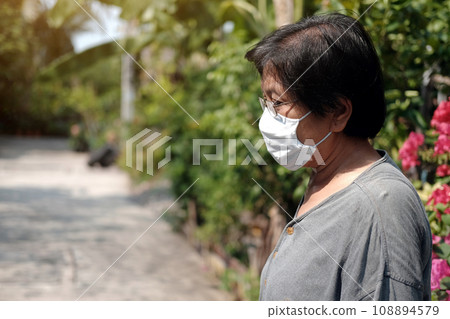 Asian old woman wearing glasses and white cloth mask for prevent the Covid-19 or Corona virus in Thailand and protect for Air Pollution Value Pm 2.5. Health and medicine of elderly in garden concept 108894579