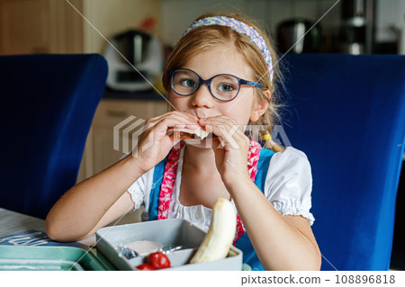Cute Little Girl with Eyeglasses Eating Sandwich and Fruits during Break between Classes. Healthy Unhealthy Food for Kid. Breakfast Lunch Box for Children at School. 108896818
