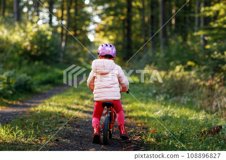 Child riding balance bike. Kids on bicycle in sunny forest. Little girl enjoying to ride glider bike on warm day. Preschooler learning to balance on run bicycle in safe helmet. Sport activity 108896827