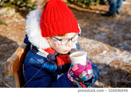 Little cute preschool girl drinking hot children punch or chocolate on German Christmas market. Happy child on traditional family market in Germany, Laughing boy in colorful winter clothes Little cute preschool girl drinking hot children punch or chocolate on German Christmas market. Happy child on traditional family market in Germany, Laughing boy in colorful winter clothes 108896846
