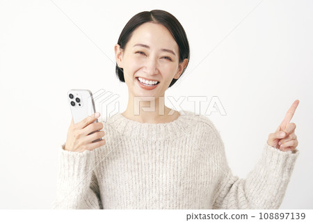 拿著智慧型手機並指向右側的中年婦女，白色背景 108897139