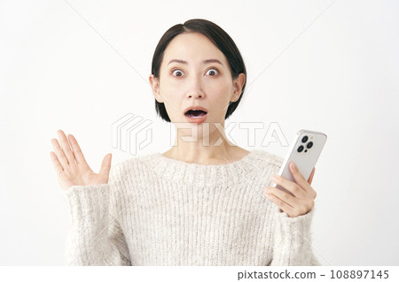 Surprised middle-aged woman holding a smartphone, white background Surprised middle-aged woman holding a smartphone, white background 108897145