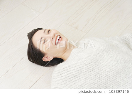 A woman lying on her back on the wooden floor in the living room 108897146