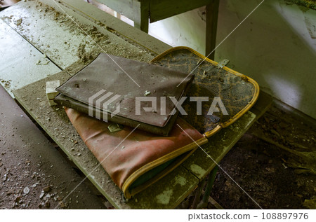 Old dirty school bag and folder for papers on desk in abandoned elementary school in village of Dronki in exclusion zone of Chernobyl, Belarus 108897976