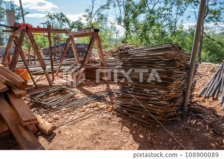 Big pile of reinforced steel bar, rebar, and stacked wood was left messily at a work site on a sunny day. 108900089