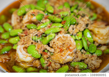 Close up Thai Stir-Fried Stink Beans with Shrimps and spicy shrimp paste sauce in white dish bowl on dark wood table. Close up Thai Stir-Fried Stink Beans with Shrimps and spicy shrimp paste sauce in white dish bowl on dark wood table. 108900091