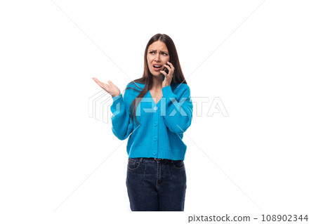 young beautiful European brunette woman dressed in a blue cardigan speaks on the phone while 108902344