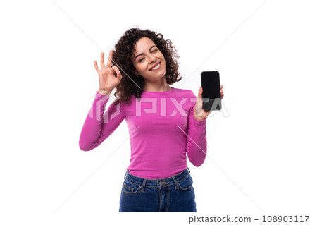 young curly promoter woman dressed in a lilac turtleneck shows the smartphone screen 108903117