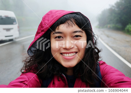 Smiling young Asian woman is travel and selfie in tropical rain forest and raining with fog on the road on vacation in Thailand Smiling young Asian woman is travel and selfie in tropical rain forest and raining with fog on the road on vacation in Thailand 108904044