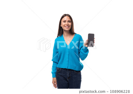 young pretty european brunette woman dressed in a blue cardigan holding a smartphone with a mockup young pretty european brunette woman dressed in a blue cardigan holding a smartphone with a mockup 108906228