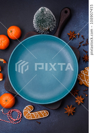 Beautiful festive Christmas composition of an empty plate, tangerine and gingerbreads Beautiful festive Christmas composition of an empty plate, tangerine and gingerbreads 108907455