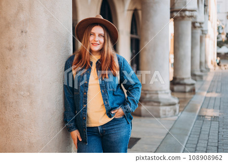 Attractive young female tourist is exploring new city. Redhead girl in hat posing on Market Square in Krakow. Traveling Europe in autumn. High quality photo, The Cloth Hall Attractive young female tourist is exploring new city. Redhead girl in hat posing on Market Square in Krakow. Traveling Europe in autumn. High quality photo, The Cloth Hall 108908962