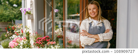 Smiling woman florist small business owner standing with crossed arms near own floral store Smiling woman florist small business owner standing with crossed arms near own floral store 108909727
