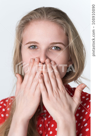 Blond woman covers mouth with hands, looking at camera. Authentic female in red polka dot dress Blond woman covers mouth with hands, looking at camera. Authentic female in red polka dot dress 108910890