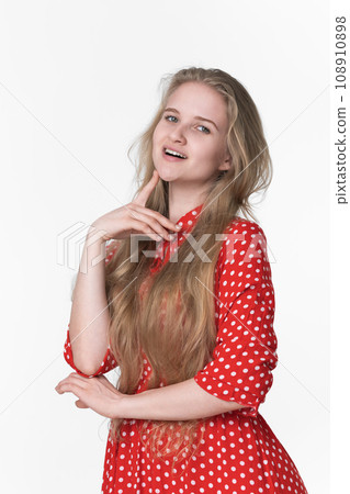 Playful young blonde female with long hair dressed in red polka dot dress poses on white background Playful young blonde female with long hair dressed in red polka dot dress poses on white background 108910898
