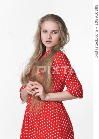 Elegant young blonde female with long hair dressed in summer red polka dot dress on white background 108910899
