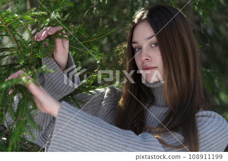 Portrait of teenager with long hair, without make-up looking at camera on background pine woodland 108911199