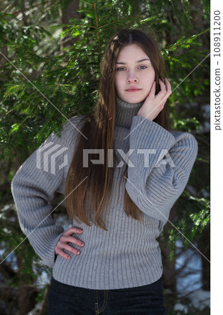 Portrait of teenager girl standing in pine forest. Brunette teenager in sweater looking at camera Portrait of teenager girl standing in pine forest. Brunette teenager in sweater looking at camera 108911200