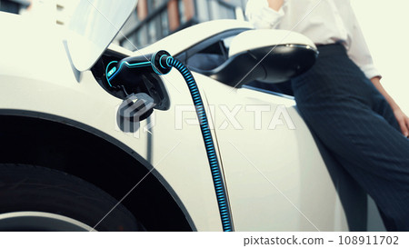 Businesswoman recharge her electric car from charging station. Peruse Businesswoman recharge her electric car from charging station. Peruse 108911702