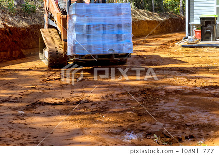 As worker works with small forklift he is unloading pallets of concrete blocks for retaining wall As worker works with small forklift he is unloading pallets of concrete blocks for retaining wall 108911777