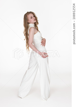 Back view of young woman looking over shoulder at down wearing long jumpsuit standing in full length 108912554