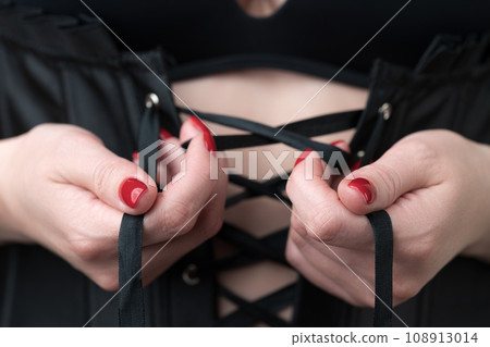 Female hands lacing up ties on corset on her front. Extreme closeup. Depth of field, selective focus Female hands lacing up ties on corset on her front. Extreme closeup. Depth of field, selective focus 108913014