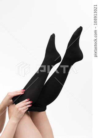 Closeup view of female hands putting on black pantyhose. Crop view of woman legs on white background 108913021