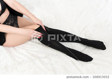 Adult woman carefully dressing black tights over her legs. Crop view unrecognizable woman on bed Adult woman carefully dressing black tights over her legs. Crop view unrecognizable woman on bed 108913032