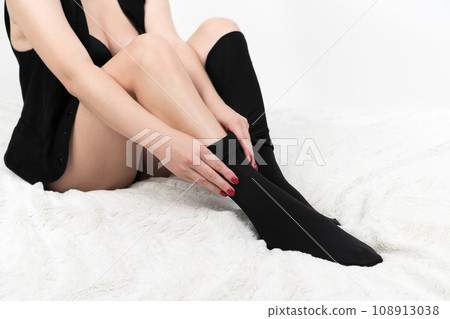 Cropped view of woman carefully dressing black tights over her legs. Unrecognizable female on bed Cropped view of woman carefully dressing black tights over her legs. Unrecognizable female on bed 108913038