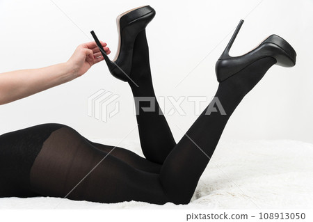 Woman in tights and high heels lies with legs bent in knees and raised up. Hand holds shoes by heel Woman in tights and high heels lies with legs bent in knees and raised up. Hand holds shoes by heel 108913050