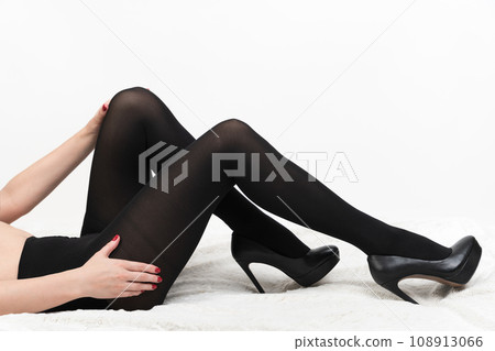 Female in black tights and high heel shoes lying on back, legs bent at knees, hands on hip and knee 108913066