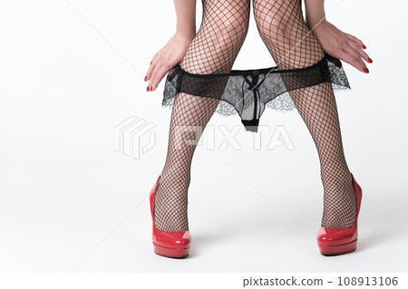 Woman pulls knickers down to knees with both hands. Female legs in red high heels shoes, stockings 108913106