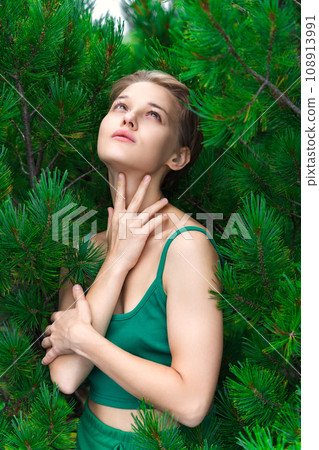 Portrait of blonde woman with short hair looking up, poses on background of shrub of Pinus Pumila Portrait of blonde woman with short hair looking up, poses on background of shrub of Pinus Pumila 108913991