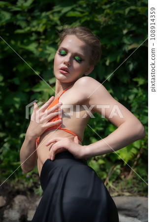 Female with eyes closed posing on background green summer foliage. Sexy woman in orange bikini top Female with eyes closed posing on background green summer foliage. Sexy woman in orange bikini top 108914359