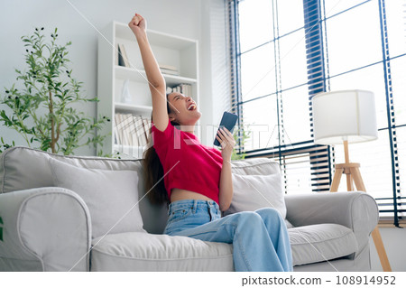 Happy young asian woman relax on comfortable couch at home texting messaging on smartphone Happy young asian woman relax on comfortable couch at home texting messaging on smartphone 108914952
