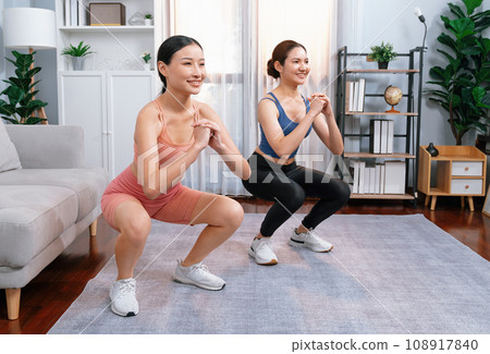 Vigorous energetic woman with trainer doing exercise at home with sport band. Vigorous energetic woman with trainer doing exercise at home with sport band. 108917840