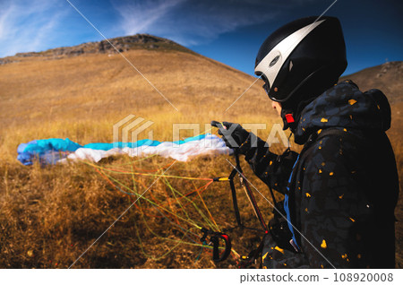 paraglider lands or rises on the yellow grass on a sunny day. A man after or before a paragliding flight. Glider with parachute, wide angle rear view 108920008