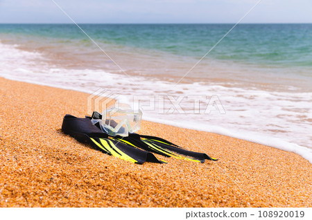 diving goggles, snorkel and fins on the beach with yellow sand. close-up of snorkeling equipment, against the backdrop of sea waves 108920019