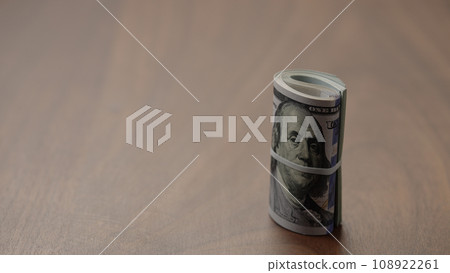 Roll of hundred dollar bills on walnut table shot Roll of hundred dollar bills on walnut table shot 108922261