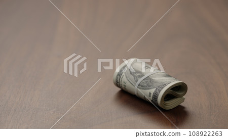 Roll of hundred dollar bills on walnut table   shot 108922263