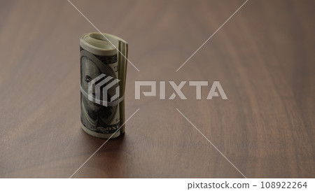 Roll of hundred dollar bills on walnut table   shot 108922264