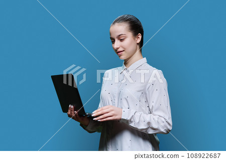 Serious teenage high school student girl using laptop on blue background Serious teenage high school student girl using laptop on blue background 108922687